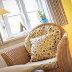 Wicker-Sofa mit blau-gelben Kissen vor Fenster mit Vorhängen.