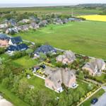 Dorf mit strohgedeckten Häusern und grünen Wiesen, gelbes Rapsfeld im Hintergrund.