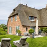 Haus mit Strohdach, Garten und Außensitzgelegenheiten.