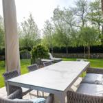 Terrasse mit Tisch und Sitzgruppe, umgeben von Grünfläche und Bäumen.