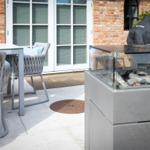Terrasse mit Sitzgruppe und Feuerkamin. Hintergrund: Haus mit Backsteinwand und Fenstern.