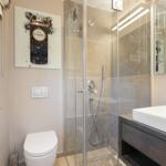 Badezimmer mit Dusche, Waschbecken und Toilette. Wandbild und Handtücher sichtbar.