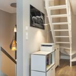 Haus mit weißen Treppen und moderner Beleuchtung. Auf einem Schrank steht ein Drucker.