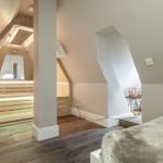 Dachgeschosszimmer mit Sauna und Bett. Holzfußboden und weiße Wände.