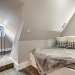 Ein Schlafzimmer mit Dachschräge, Bett mit Decke und Kissen, Stehlampe und Holzboden.