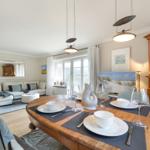 Dining room with wooden table, chairs, and window view. Living area with sofa and mirror.