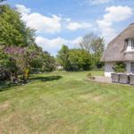 House with thatched roof, garden with lilac tree and terrace with seating area.