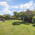 Green garden with terrace, flowers, and trees under blue sky.