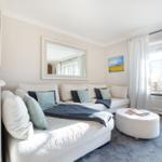 A living room with a white sofa, round ottoman, and large windows.