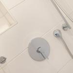 Dusche mit Chromarmatur und Handbrause an weißen Fliesen