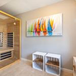Sauna mit Glaswand, Wandbild mit Segelbooten und weiße Holzstühle.