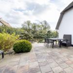 Terrasse mit Tisch, Stühlen und Gartenanlage neben einem Haus mit Schieferdach.
