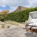 Terrasse mit Strandkorb und Tisch, Hintergrund mit Hecke und Strohdach.