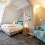 Schlafzimmer mit Bett, Sessel und Wandbild unter Dachschrägen.