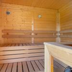 Holzsauna mit Sitzbänken und Temperaturanzeige an der Wand.