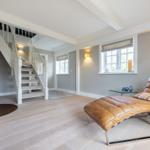 Wohnbereich mit Holzboden, brauner Ledercouch, Kamin und Treppe.