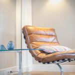 Brown leather lounge chair with patterned cushion beside glass table.