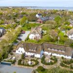 Traditionelles Ferienhaus mit Strohdach und Garten. Blick auf Küstenort mit Wasser im Hintergrund.