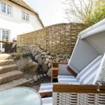 Weißer Strandkorb mit Streifenkissen im Garten vor einem Haus mit Steintreppe.