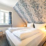 Schlafzimmer mit Bett, Fenster und Tapete mit Bambusmotiv.