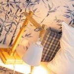 Nachtisch mit Holzlampe und Kissen vor blau-weißem Tapetenmuster.