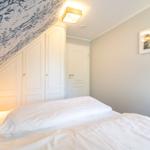 Schlafzimmer mit weißem Bett, Kleiderschrank und gemusterter Decke.