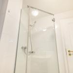 Dusche mit Glaswand, weiße Fliesen und goldener Türknauf.
