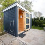 Außenliegende Sauna mit Holztür und Duschvorrichtung im Garten.
