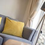 Ein grauer Sofa mit zwei gelben Kissen und einer Stehlampe neben einem Fenster.
