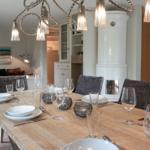 Dining area with wooden table, chairs, and pendant lights. Living room and kitchen in background.