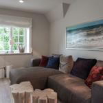 A living room with a gray sofa, a window, and a wall painting.