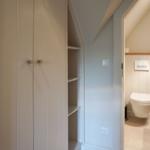 Bedroom with wardrobe and view into bathroom with toilet and sink.
