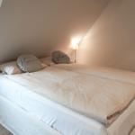 Bedroom with double bed, two pillows with text, and standing lamp.