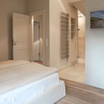 Bedroom with bed, door, and bathroom. Wall picture shows beach.