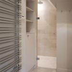 Shower with stone tiles and heater on the wall.