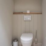 Toilet with wooden shelf, toilet paper, and brush holder