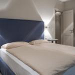 Bedroom with double bed, blue headboard, and nightstands. View into the bathroom.