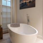 Freestanding bathtub with shower faucet and window with blinds.