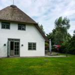 White house with thatched roof, garden and terrace with table and chairs.