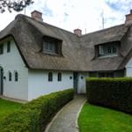 White house with thatched roof and manicured garden.