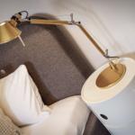 Graue Couch mit weißen Kissen und goldener Stehlampe auf weißem Beistelltisch.