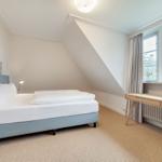 Schlafzimmer mit Dachschräge, Bett, Schreibtisch und Fenster.