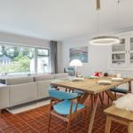 Wohn- und Essbereich mit Holztisch, blauen Stühlen und Terrasse. 