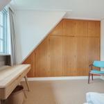Schlafzimmer mit Holzschrank, Schreibtisch und blauer Sitzgelegenheit.