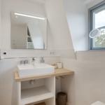 Badezimmer mit Waschbecken, Spiegel und Fenster.