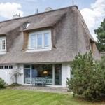Haus mit strohgedecktem Dach und weißen Wänden, umgeben von Grünflächen und Bäumen.