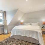 Bedroom with sloped ceiling, bed, nightstand, and window.