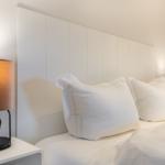 Bedroom with white bed, headboard, and nightstand with lamp.