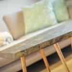 A table with wooden legs and a metallic-looking top in front of a sofa.
