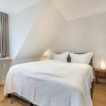 Bedroom with sloped ceiling, window, and bed with white pillows.